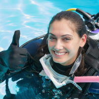 Smiling woman on scuba training in swimming pool showing thumbs up on a sunny day